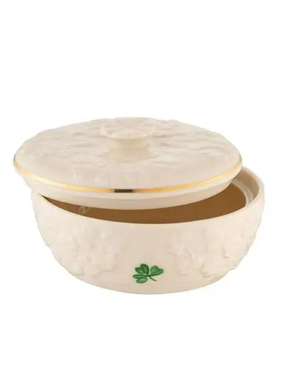 An elegant, round, ivory-colored ceramic dish with a textured surface and a shamrock clover motif, featuring a decorative lid with a floral knob and a gold trim.